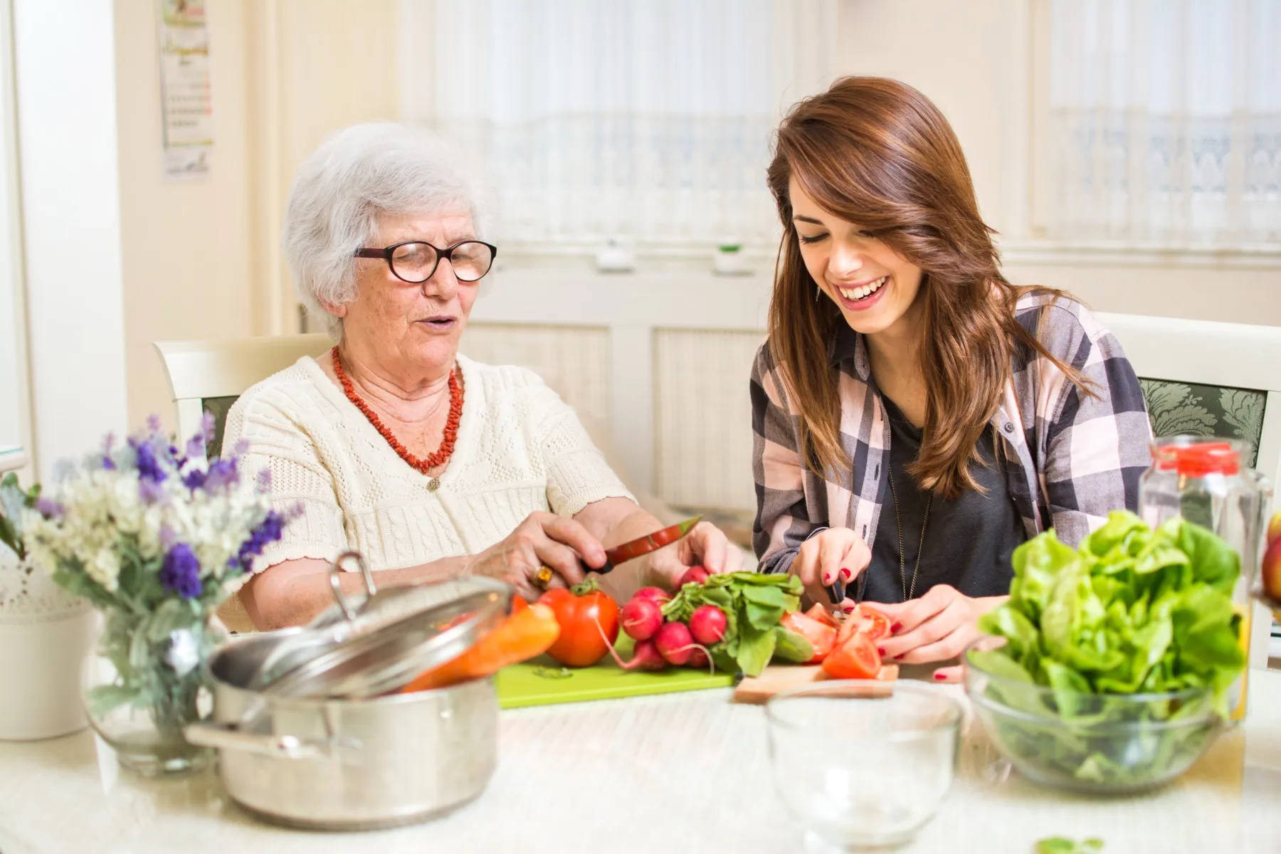 A caregiver and a senior cooking together in the kitchen at home
